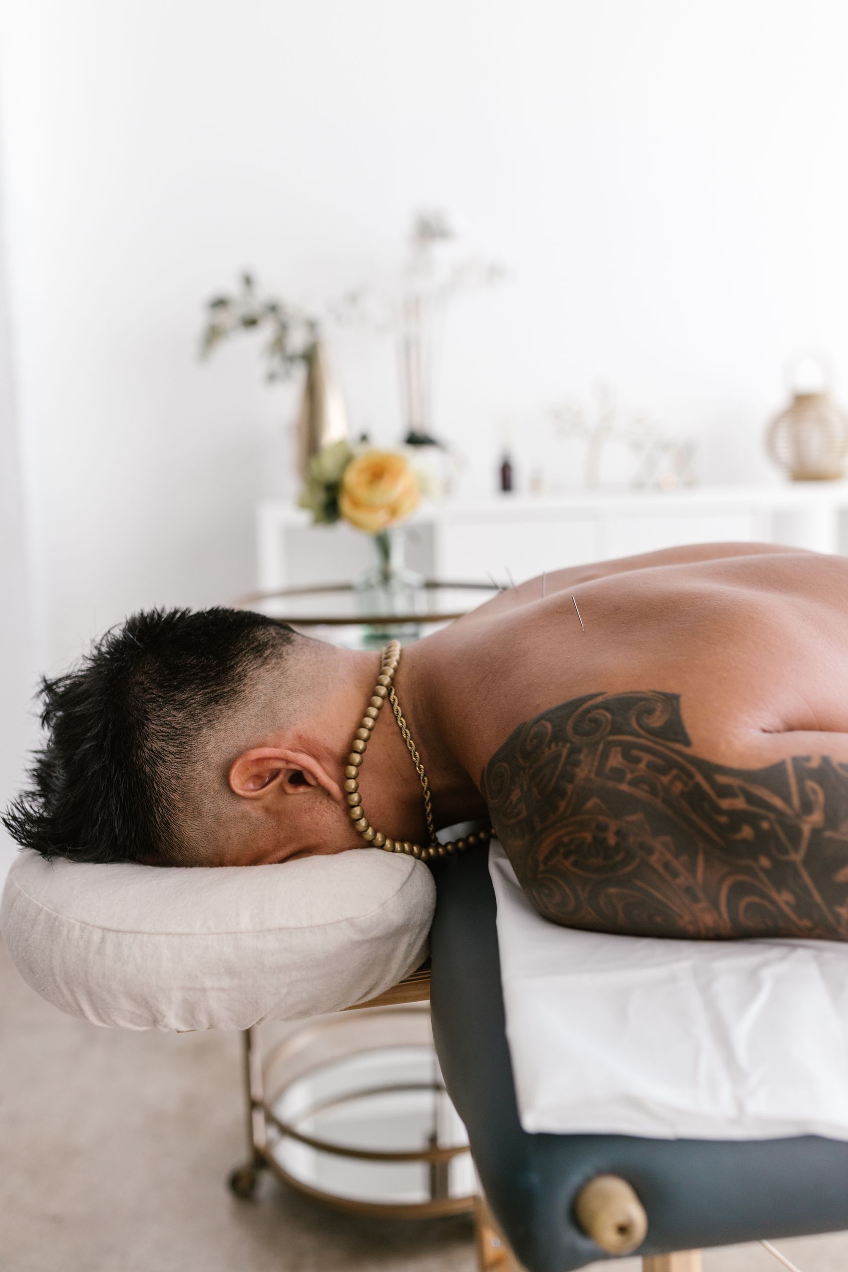 Tattooed man lying face down on a massage table in a spa setting for relaxation and wellness.